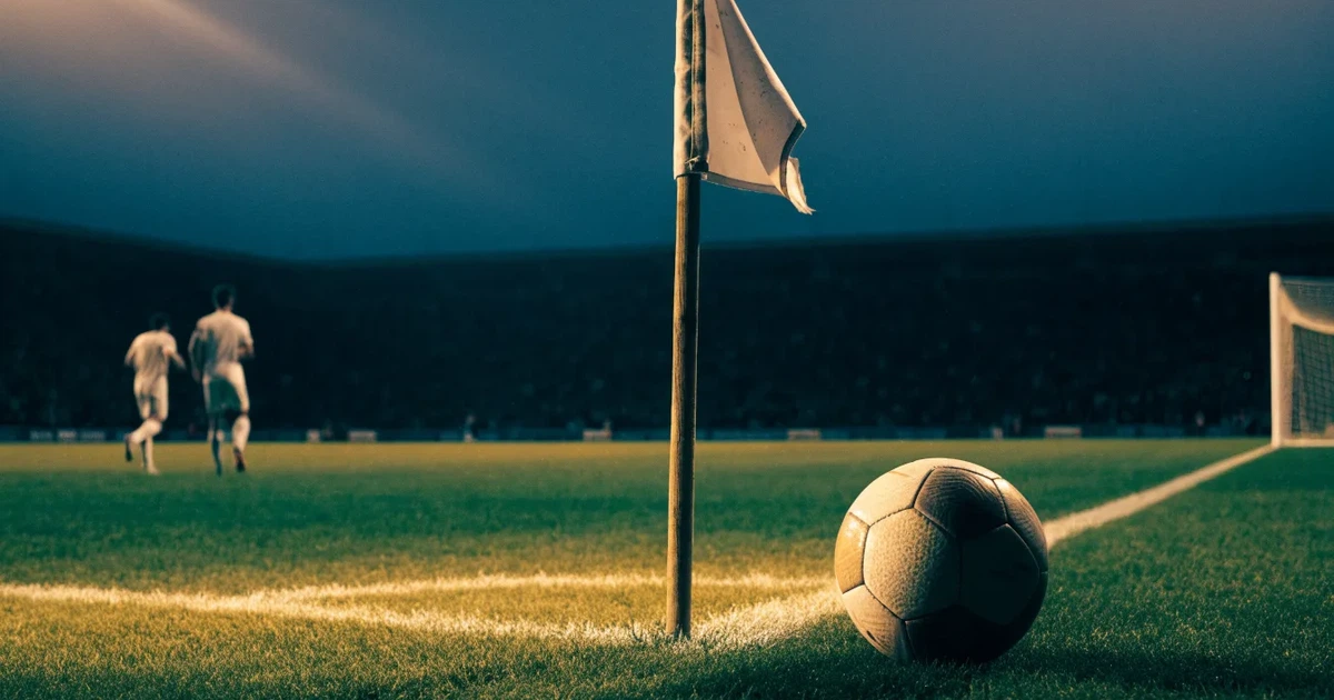 Blick durch ein Stadiontor auf einen grünen Rasen im Abendlicht, ein Ball ruht an der Eckfahne, die Tribünen sind leer.