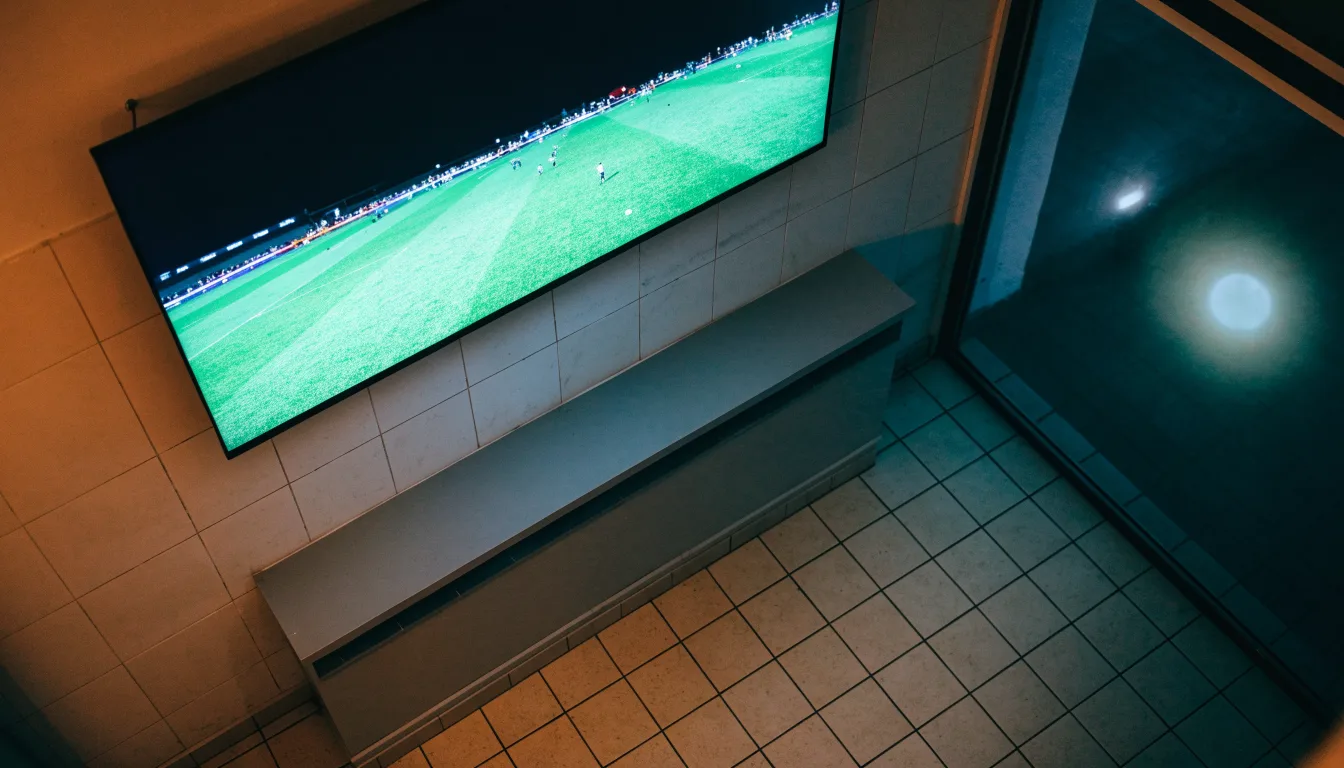 Ein Stadion unter Flutlicht aus der Ferne gesehen, im Vordergrund ein ruhiger Fluss und ein Fußweg.